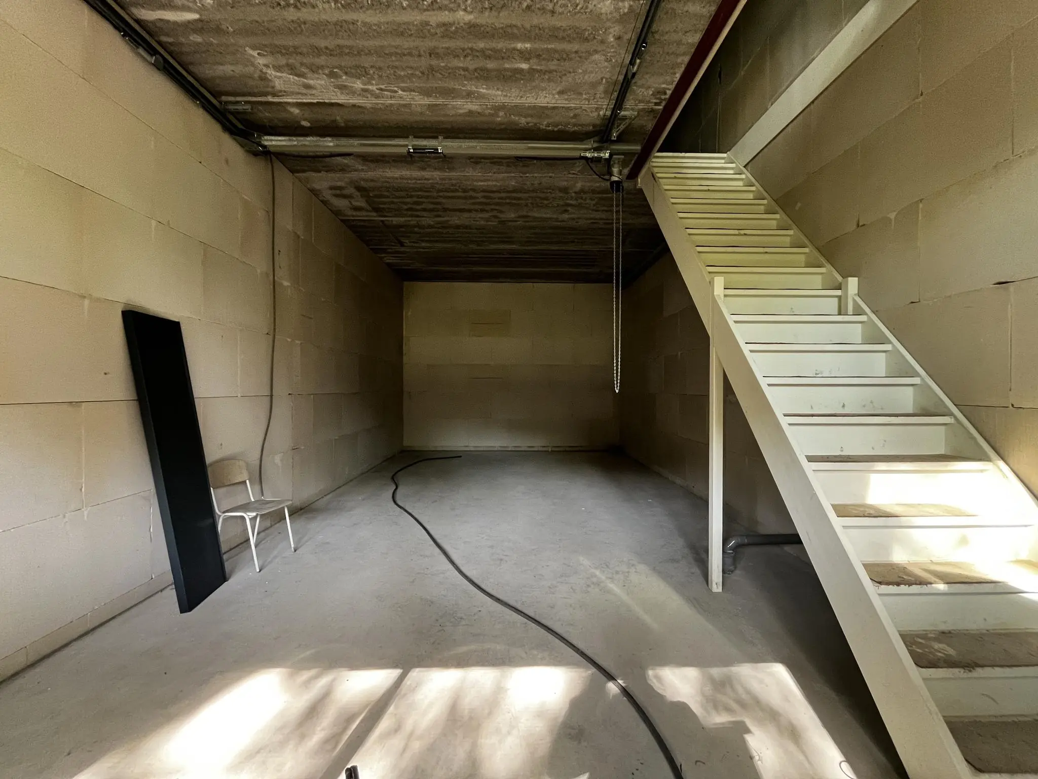 Lege opslagruimte aan de Broekdijk West 19-10 met betonnen muren, een witte trap en een stoel tegen de muur.